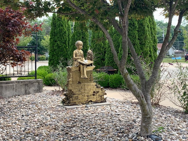 A statue of Boy and girl reading on top of a brick wall with rocks on the ground and evergreens behind. Stands outside of Children's area at the Louis Latzer Public Library in Highland, IL.