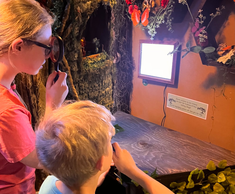 A boy and girl use a magnifying glass to look at a hologram on a screen at Adventures of Intrigue in Saint Louis, Missouri.