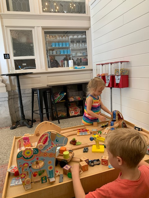 Little girl and boy playing with wooden toys and train set on table at Post Commons coffee shop in Alton, IL