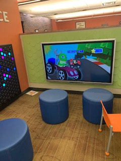 Roxana Illinois Library kids room with a screen for interactive gaming, children's seats, and an interactive lightup board.